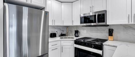 A modern kitchen with white cabinets, stainless steel appliances, a built-in oven, and a microwave.