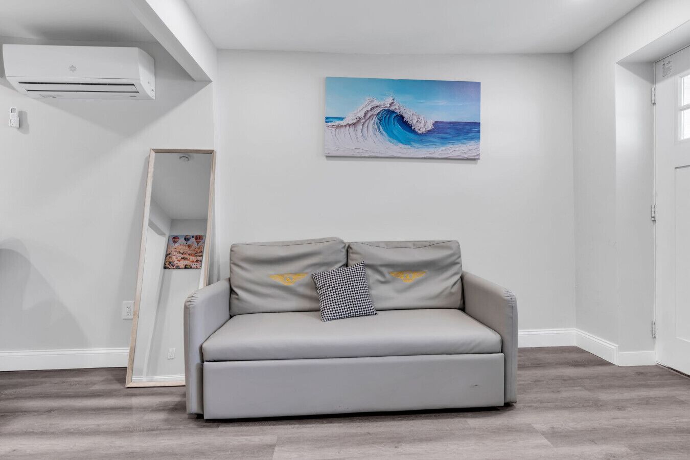 Un canapé gris avec un coussin à carreaux et un tableau représentant une vague accroché au mur.