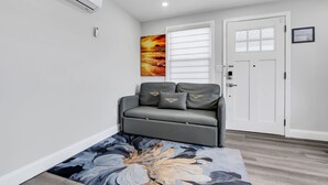 A modern living room with a grey sofa, a large abstract painting, and a wooden floor. - 1BR, Free Parking, Steps to the Boardwalk (Seaside Heights)