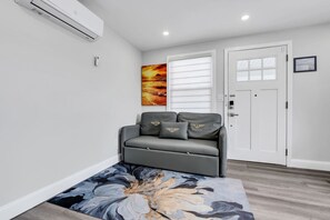 Una sala moderna con un sofá gris, un cuadro abstracto grande y piso de madera.