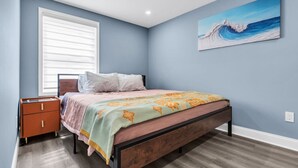 Une chambre à coucher avec un lit, une table de chevet et un tableau représentant une vague accroché au mur.