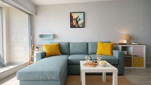 En moderne stue med en hjørnesofa, et sofabord med snacks, en lampe og et billede på væggen.