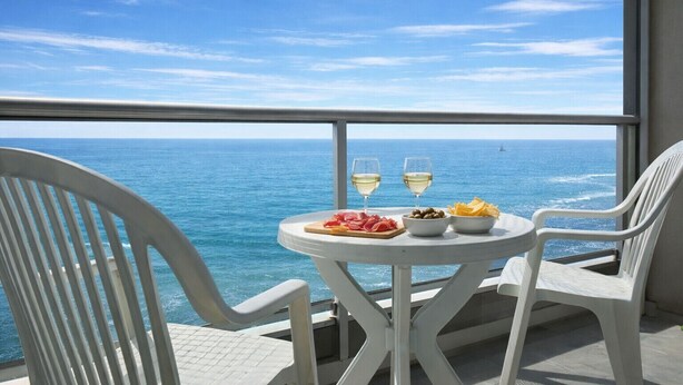 En balkon med et bord dækket til to, med udsigt over havet.