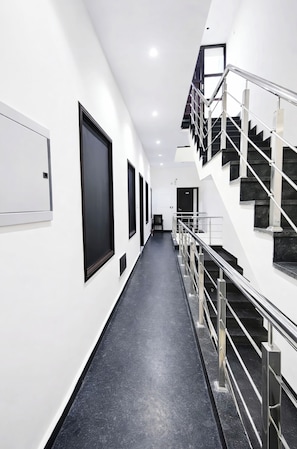 Un pasillo moderno de hotel con una escalera, puertas con marco negro y barandilla de metal.