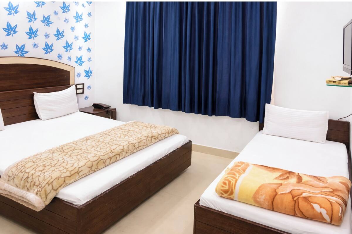 A double bed with a patterned blanket, a bedside table with a phone, and a wall with leaf decals.