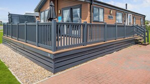 A mobile home with a deck, a covered patio, and a staircase leading to the entrance. - Deluxe 2, Slps 4, parking, ensuite, decking, HT (Burgh Castle, Great Yarmouth)