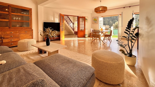 Amplia sala de estar con un aparador de madera, un televisor, una escalera que lleva a un balcón y una zona de comedor.