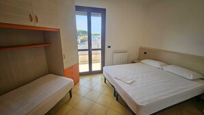 A bedroom with a bed, a bench, a wardrobe, and a sliding glass door leading to an outdoor area. - Familiar Apartment With Terrace in Rosolina (Rosolina)