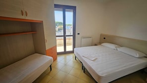 A bedroom with a bed, a bench, a wardrobe, and a sliding glass door leading to an outdoor area. - Familiar Apartment With Terrace in Rosolina (Rosolina)