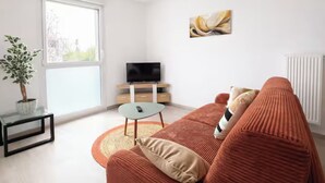 Un salon moderne avec un canapé, un téléviseur, une petite table et une plante en pot.