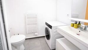 Une salle de bain moderne équipée de toilettes, d’un lave-linge et d’un lavabo avec un miroir.