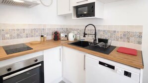 Une cuisine moderne avec des meubles blancs, un micro-ondes noir, un évier avec un robinet noir et un plan de travail en bois.