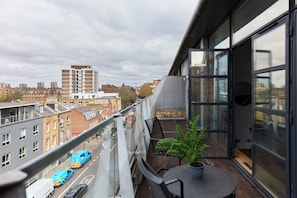 Ein Balkon mit Blick auf eine Stadtstraße, ein Tisch mit einem Blumentopf und ein Stuhl.