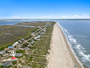 An aerial view of a coastal area with a long beach, a road parallel to the shore, and a row of houses with a red-roofed building highlighted. - D by the Sea: 4-bedroom, plus a loft with additional sleep space, oceanfront retreat (Oak Island)