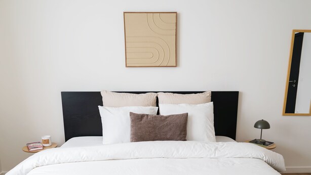 A neatly made bed with a headboard, a bedside table with a lamp, and a wall-mounted artwork. - Relaxing 5BR Apartment Close to Downtown (Ghent)