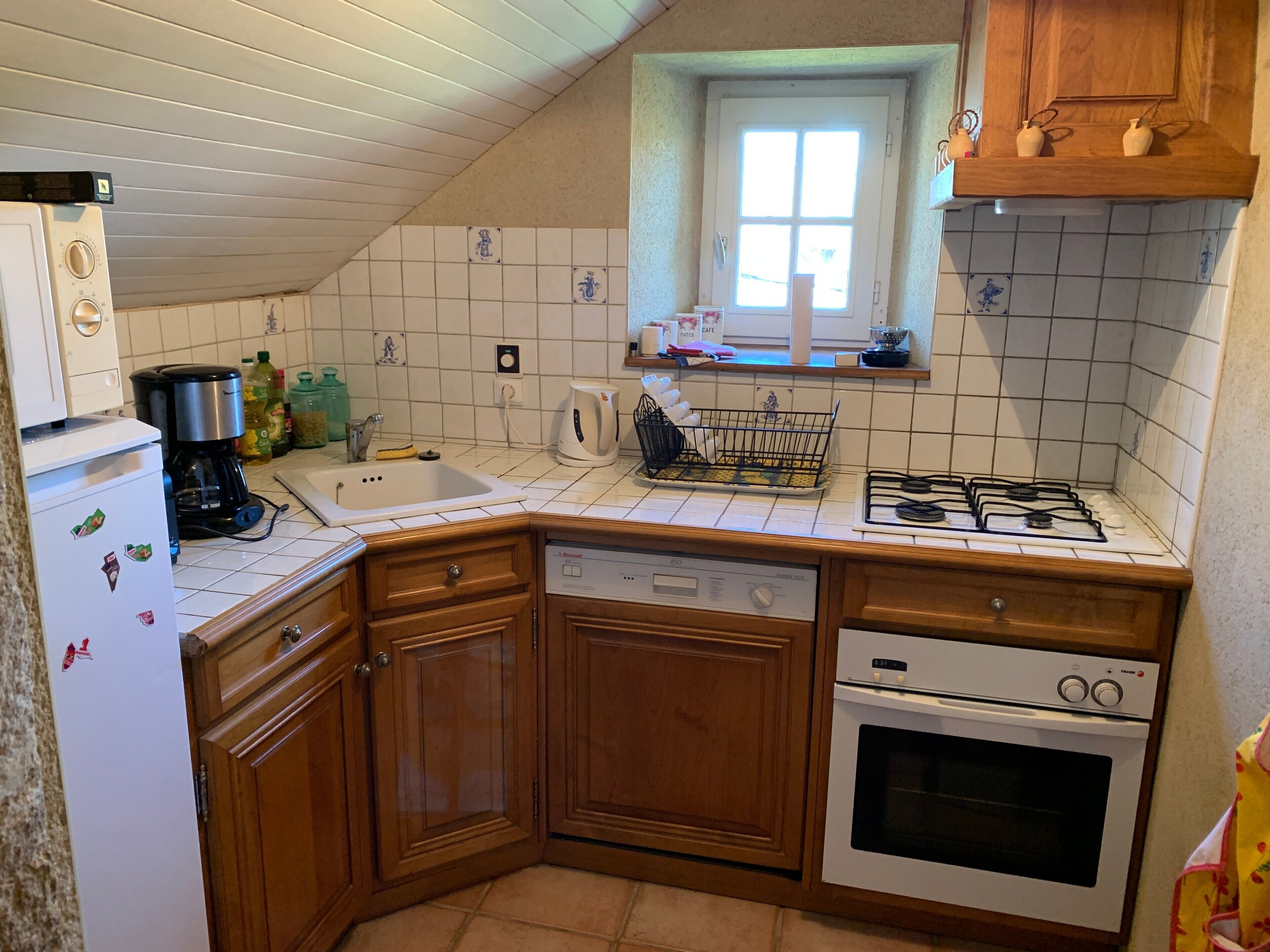 A kitchen with a refrigerator, coffee maker, sink, stove, and wooden cabinets.