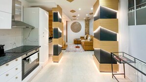 A modern kitchen with built-in appliances, a dining area with a glass table, and a living room with a sofa and a decorative wall piece. - UrbanFlat 226 - Appartement pour 6  au Centre de paris (Paris)