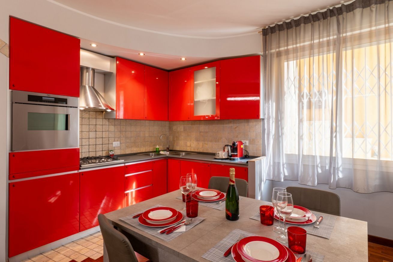 A modern kitchen with red cabinets and a dining area set for two with a table, chairs, and a bottle of champagne.