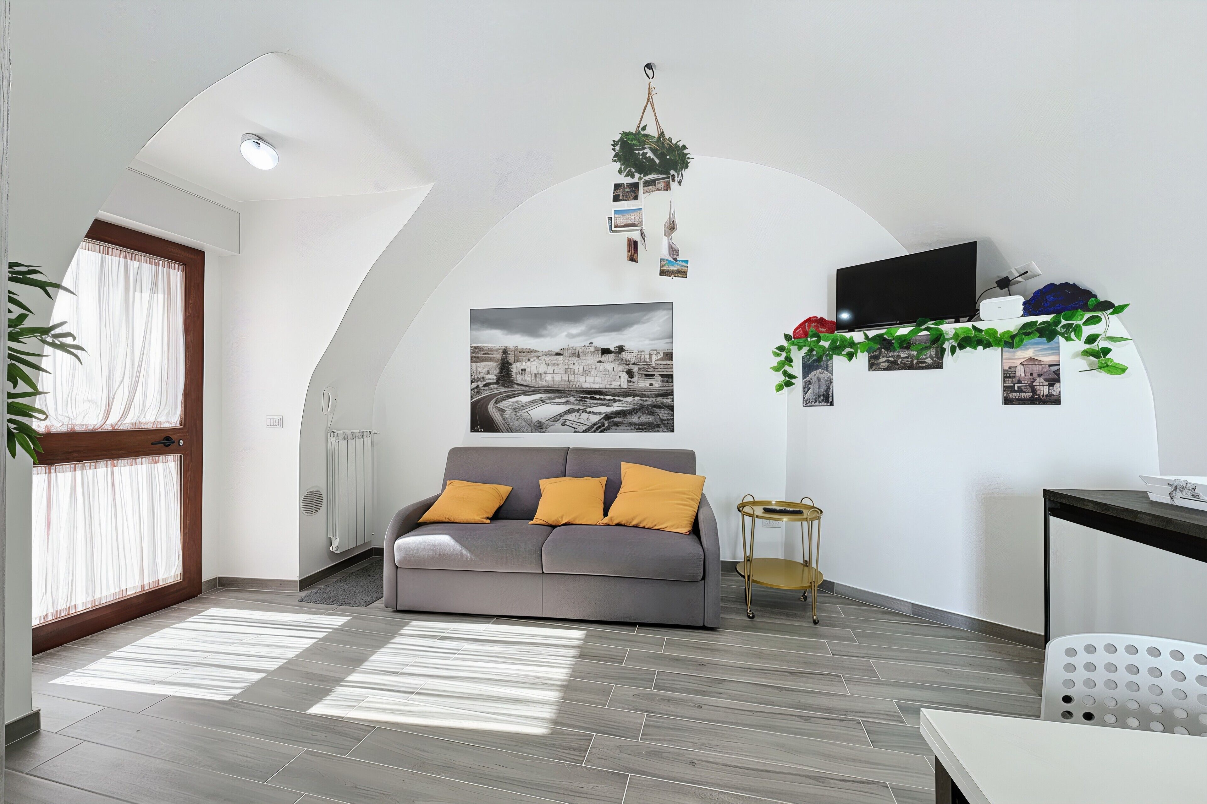 A modern living room with a grey sofa, a small side table, a TV, and a radiator.