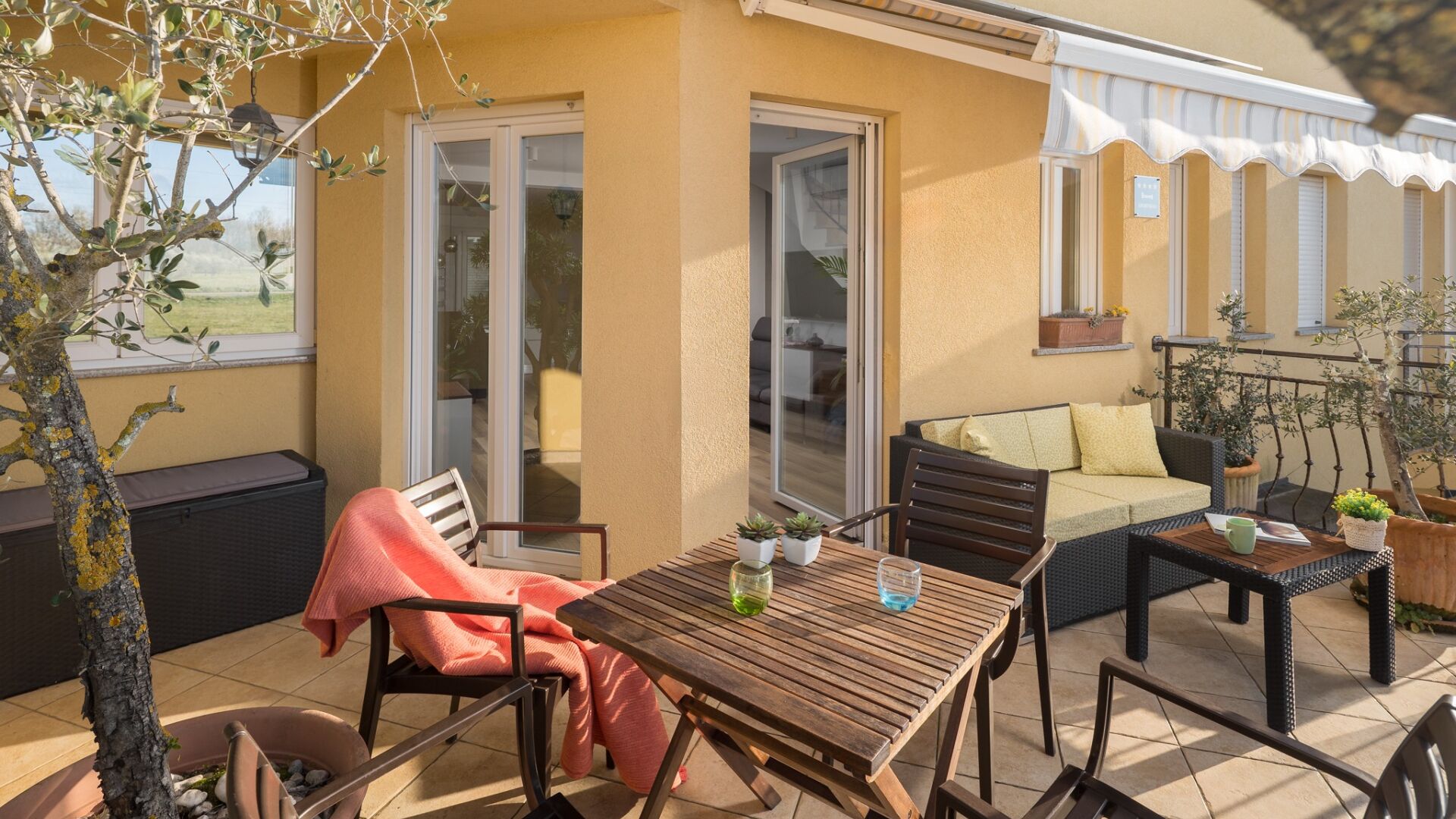En udendørs terrasse med et træbord, stole, en sofa og en lille bålplads.