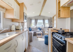 A compact RV kitchen with a stove, sink, and a dining area with a sofa. - Bronze 2 Bedroom Caravan, Sleeps 6 (Walton-on-the-Naze)