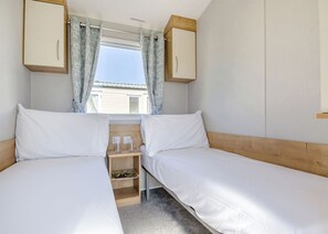Habitación doble con dos camas, una mesita de noche de madera, una ventana con cortinas y vistas al exterior.