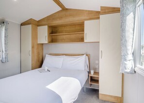 Un dormitorio con cama, mesita de noche, armario y ventana con cortinas.