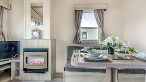 Een moderne woonkamer met een open haard, een televisie en een eethoek met een tafel gedekt voor twee personen.