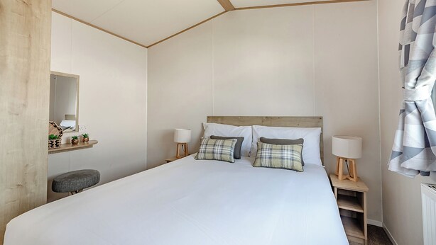 Een slaapkamer met een groot bed, nachtlampjes, een houten hoofdbord, een klein krukje, een spiegel en een plank met decoratieve objecten.