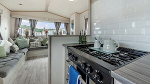 Een moderne RV-keuken met een gasfornuis, een spoelbak en een eethoek met een bank en gordijnen.