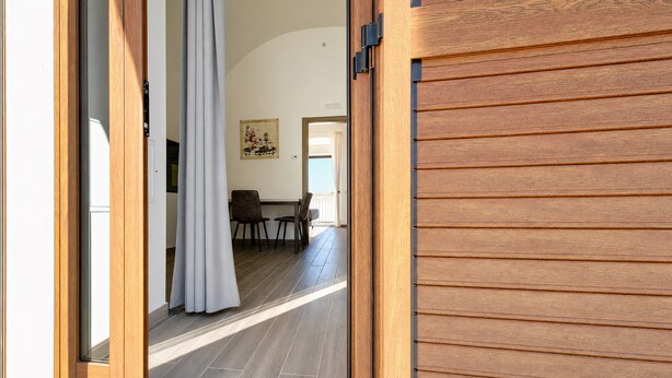An open door leading to a room with a dining table and chairs, a painting on the wall, and a view of the outdoors.