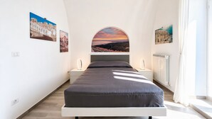 A bedroom with a bed, a nightstand, a mirror, and a view of a cityscape through an arched window.
