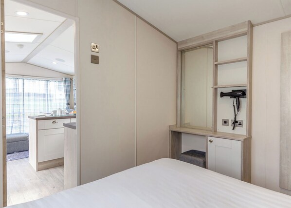 Une chambre à coucher comprenant un lit, une coiffeuse avec un miroir, un sèche-cheveux et un petit tabouret.
