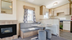 Ett kompakt bostadsutrymme med en soffa, ett litet matbord, en öppen spis och ett litet kök.