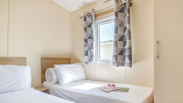 Ett hotellrum med två separata sängar, en sänggavel i trä, ett fönster med geometriskt mönstrade gardiner och ett litet bord med en bok och ett par solglasögon.