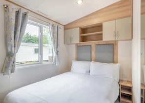 Une chambre à coucher avec un lit, des rideaux, une fenêtre et des armoires encastrées en bois.