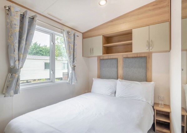 A bedroom with a bed, curtains, a window, and built-in wooden cabinets.