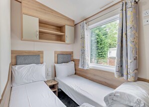 Habitación doble con cama de madera, mesita de noche, espejo y ventana con cortinas.