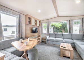 Un intérieur de camping-car moderne avec une table en bois, un canapé gris et un téléviseur fixé au mur.