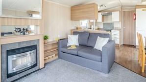 Ein kompaktes Wohnmobil-Interieur mit Küchenzeile, einem grauen Sofa, einem Kamin und einer Spiegelwand.