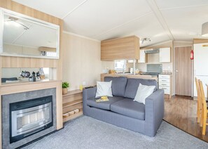 Un intérieur de camping-car compact comprenant un coin cuisine, un canapé gris, une cheminée et un mur miroir.