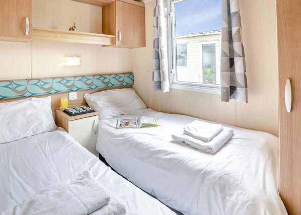 Un dormitorio con dos camas, una mesita de noche con un libro, una lámpara y una ventana con cortinas.