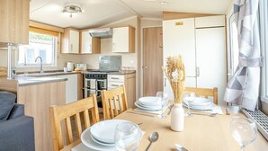 Eine kompakte Küche mit Herd, Backofen und Spüle, ein Essbereich mit Tisch für zwei Personen und ein Fenster mit Vorhängen.