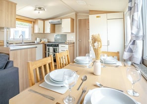 A compact kitchen with a stove, oven, and sink, a dining area with a table set for two, and a window with curtains.