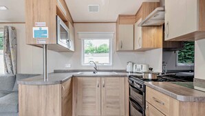 A compact kitchen with wooden cabinets, a built-in stove, and a window providing natural light. - Gold Caravan with parking P (Walton-on-the-Naze)