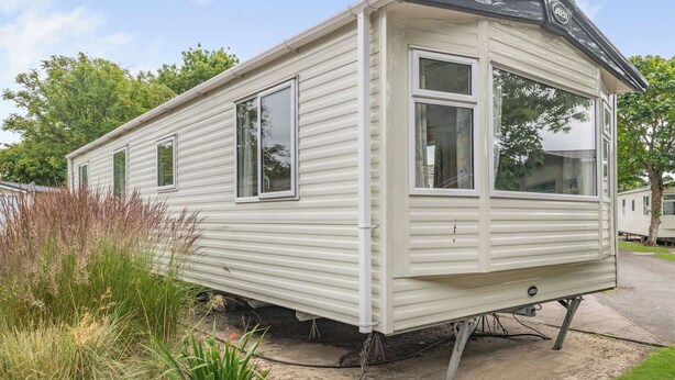 A mobile home with a single window on the side, a door, and a small porch area. - Gold Caravan with parking P (Walton-on-the-Naze)