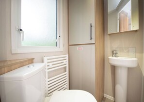 Un baño pequeño con inodoro, ventana, radiador, lavamanos y armario.