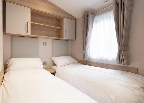 Un dormitorio con dos camas, cabeceros de madera, un armario y una ventana con cortinas.