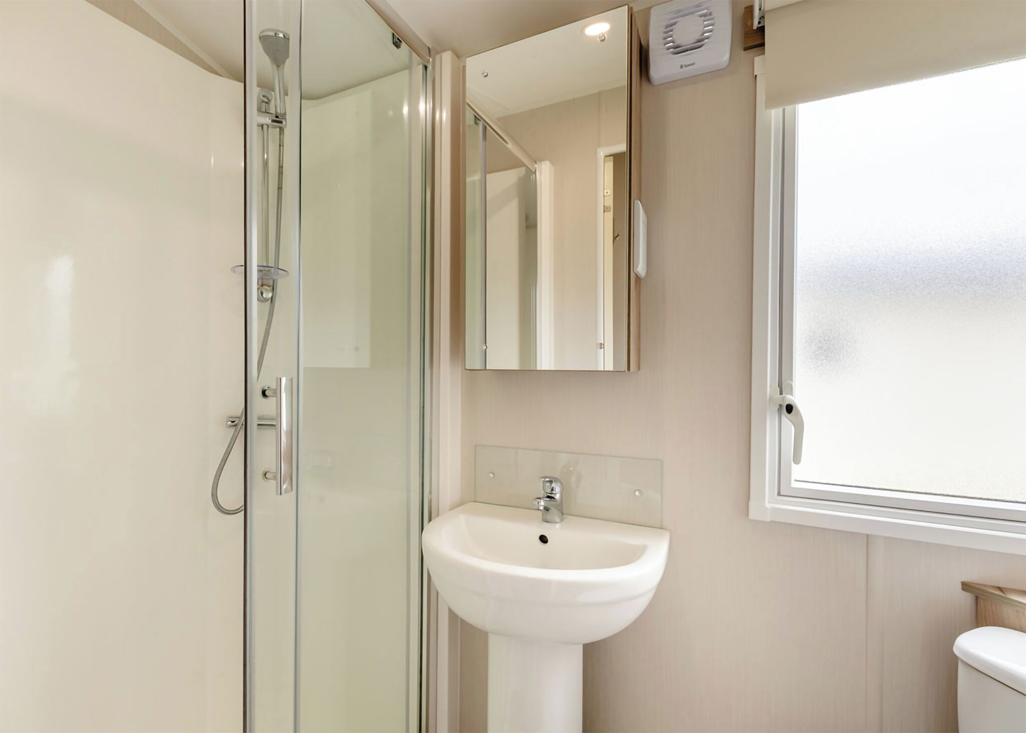 Ein Badezimmer mit Duschkabine aus Glas, einem weißen Waschbecken und einem Fenster.