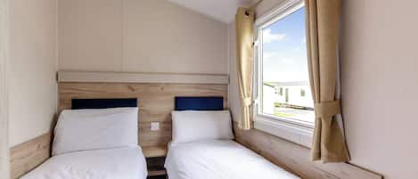 A room with two beds, a window with curtains, and a view of a building outside.